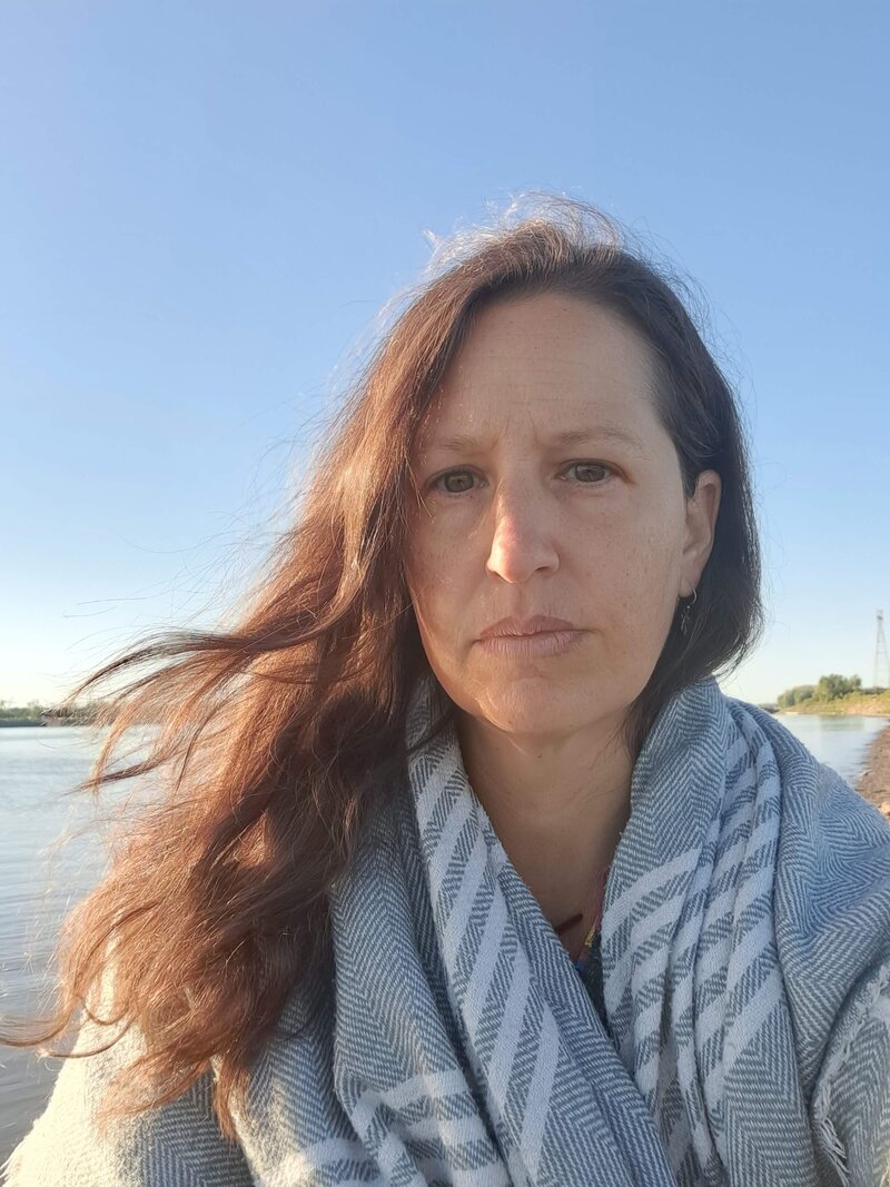 Women in golden light, wearing dark rimmed glasses and striped shirt, smiling down at her hands as she rolls out clay