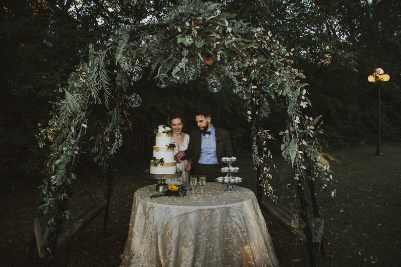 bride and groom cutting cake under flower trellis