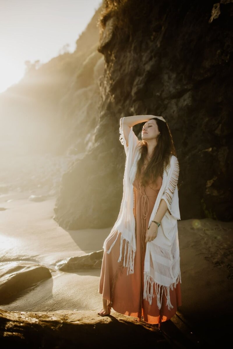 Woman with long hair stands on a sunlit shore.