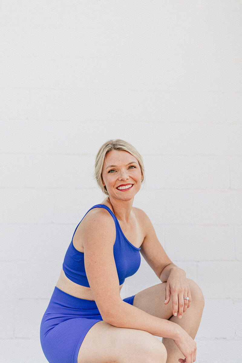 Kelsey Wickenhauser, a Christian health coach, confidently posing in blue workout attire against a clean white backdrop