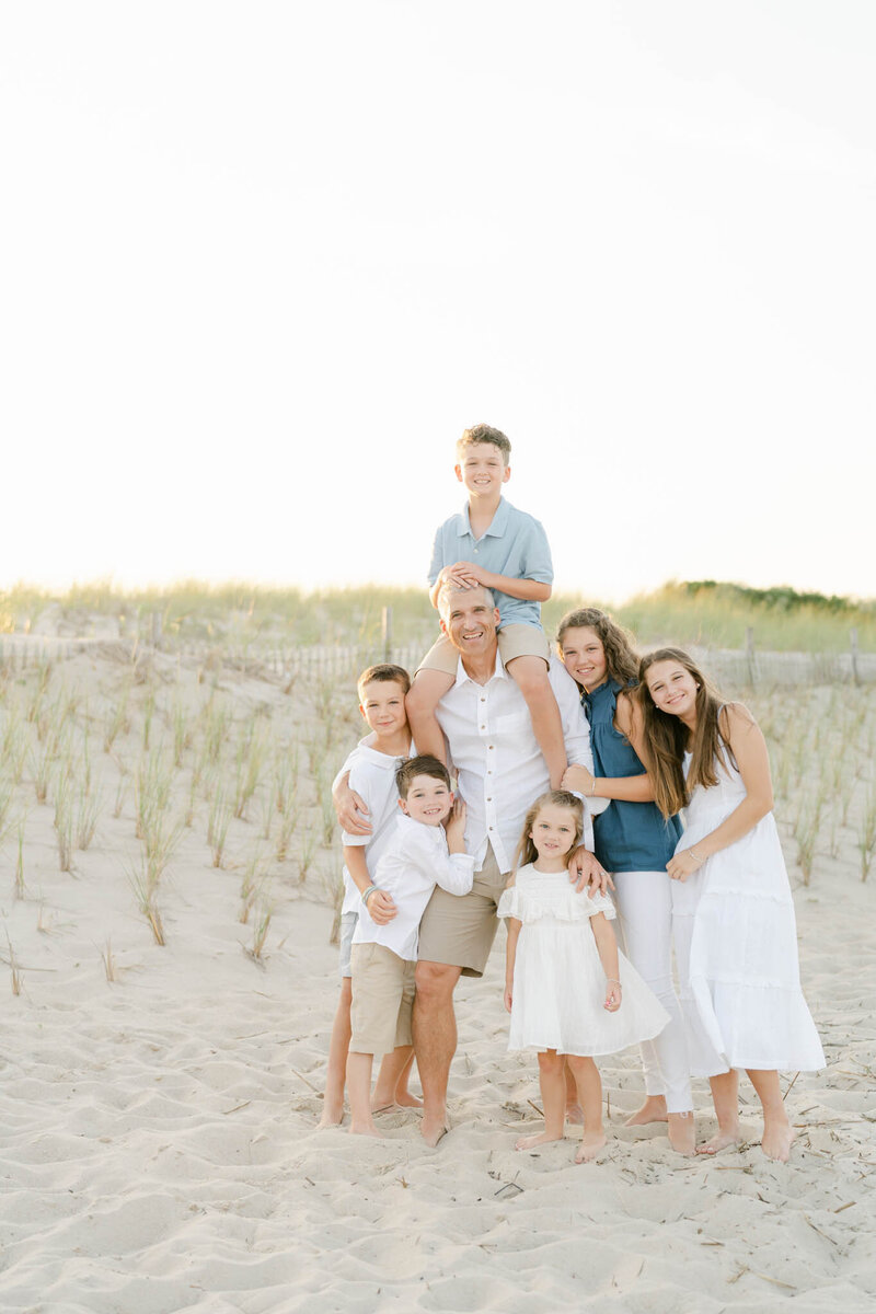 dad in white linen shirt poses with his six children on the beach in Delaware during a photo session with AnneMarie Hamant, Lifestyle Photographer