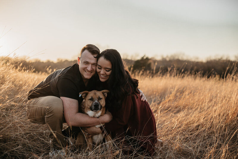Man and woman hold their dog close in grassy field
