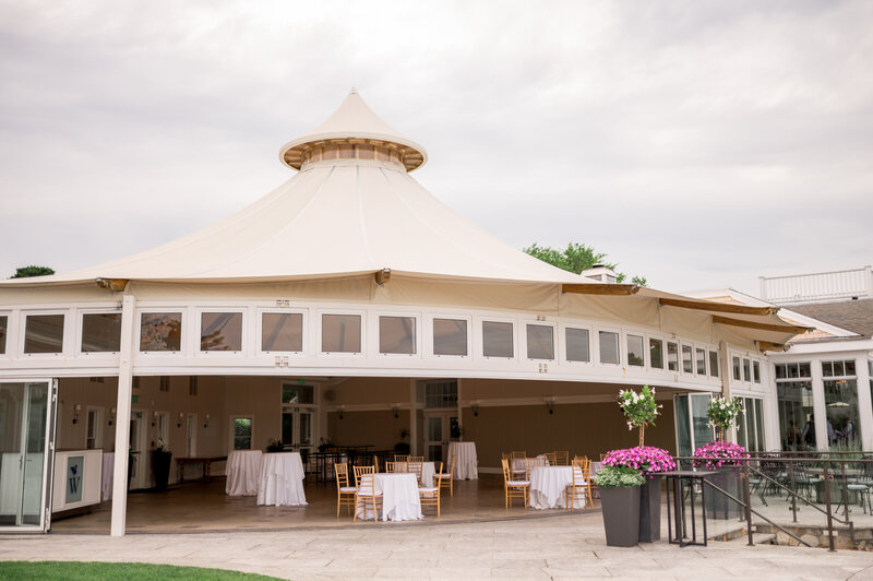 An elegant open-air tented pavilion with white paneling and gold chairs set for an event at Wequassett Resort, surrounded by summer florals and Cape Cod charm.