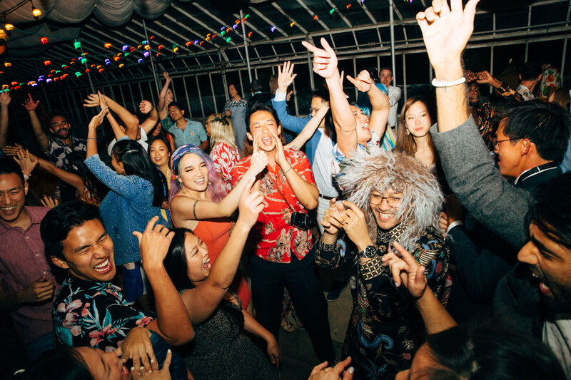 A group of cheerful and joyful wedding guests join the groom in dancing during the wedding reception in the greenhouse at Dos Pueblos Orchid Farm in Santa Barbara.