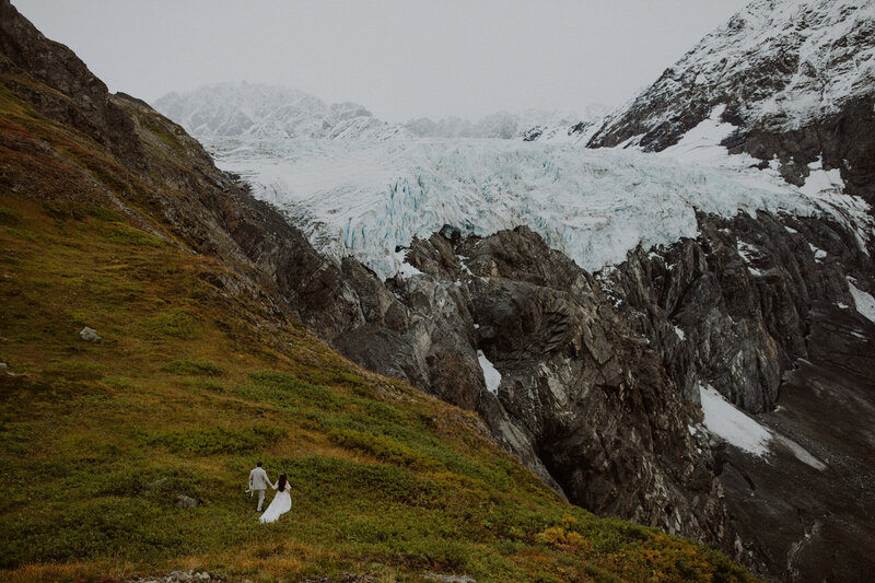 Couple walks to the edge of a cliff overlooking a giant glacier