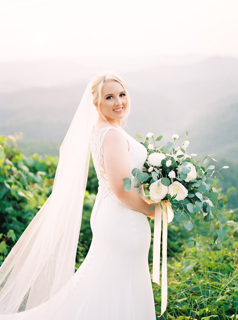 Picture of bride holding a white bouquet with cloudy mountains in the background