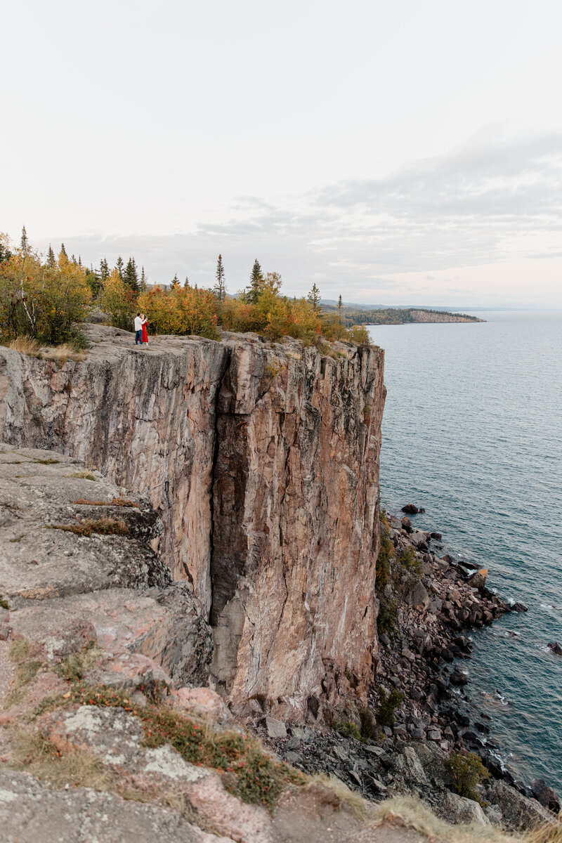 Engagement session at Palisade Head in Silver Bay, MN, part of Tettegouche State Park, featuring a couple surrounded by vibrant fall colors on the cliffs overlooking Lake Superior, captured by a wedding and elopement photographer in Duluth, MN