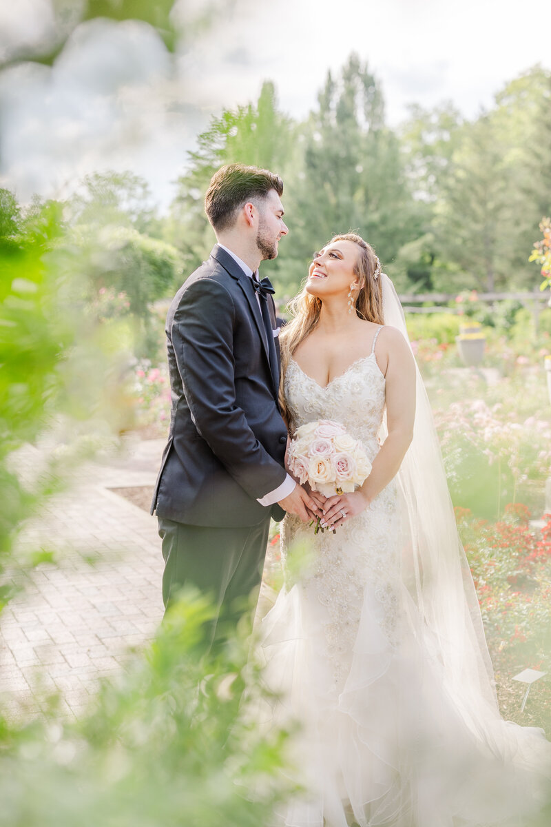 Newlyweds share an intimate moment in a garden in a black suit and lace dress and documented by a Saginaw Wedding Photographer