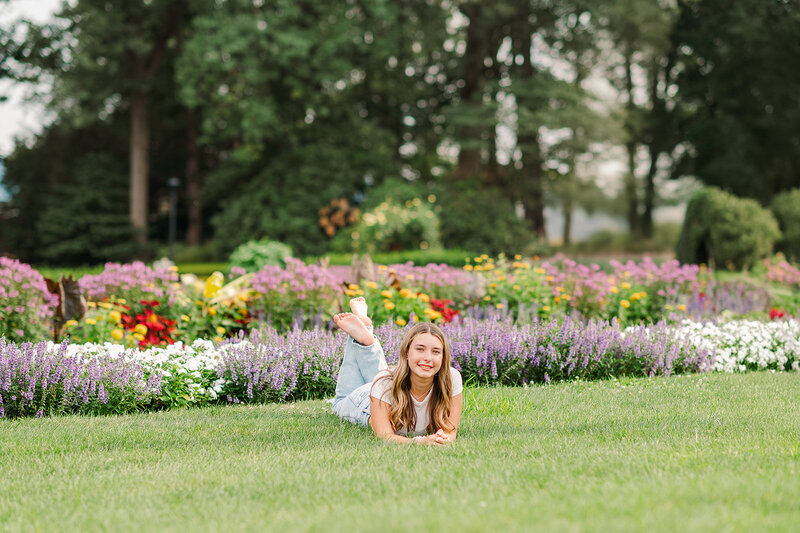 Senior girl laying in the grass in front of rows of flowers at Hershey Gardens, by Lancaster PA photographer
