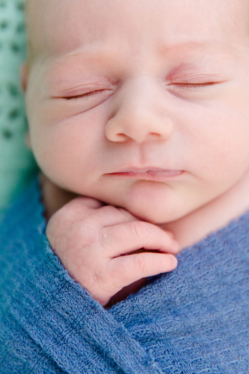 Newborn baby is swaddled and sleeping with his hand touching his face during his newborn session