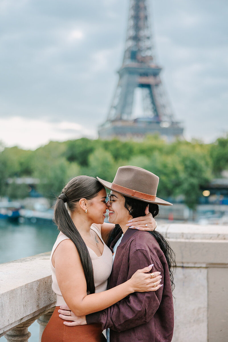 Lesbian couple laughing and kissing after a Paris proposal near the Eiffel Tower at Bir-Hakeim Bridge — captured during a romantic photoshoot by Rachael Laporte.
