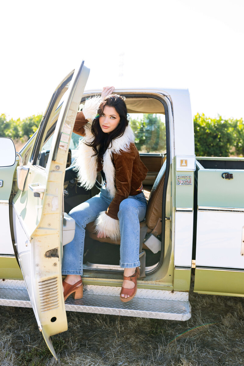 brunnete girl with fur coat getting out of vintage green and white truck and wearing brown heels