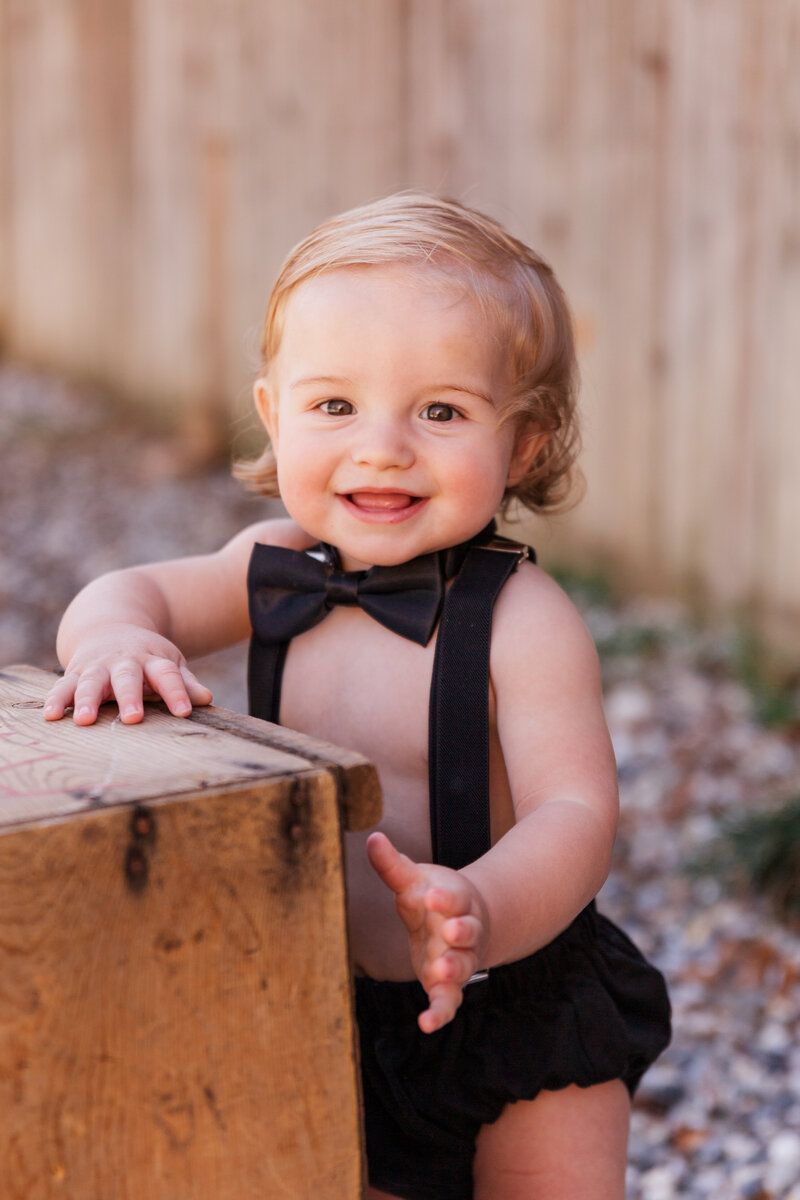 baby boy wears a black bow tie and suspenders for cake smash