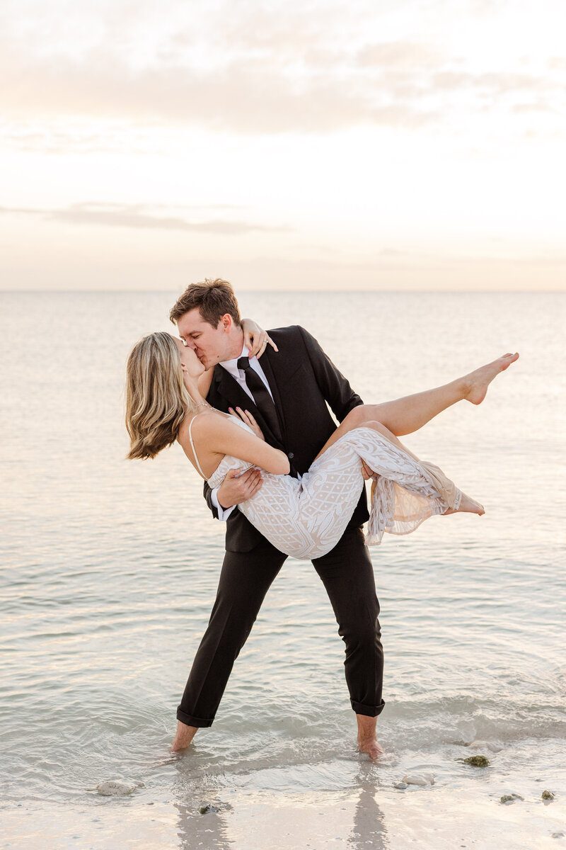 Groom holding Bride during a beach sunset sharing a passionate kiss. Photographed by Meredith Mutza Photography LLC.