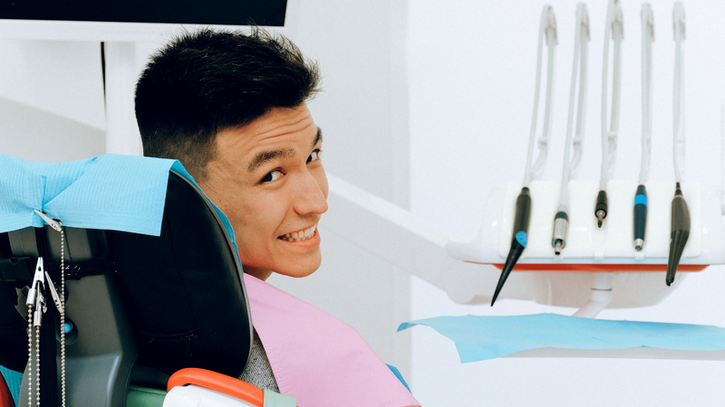 A man sitting in a dental chair looks over his shoulder at the camera smiling.
