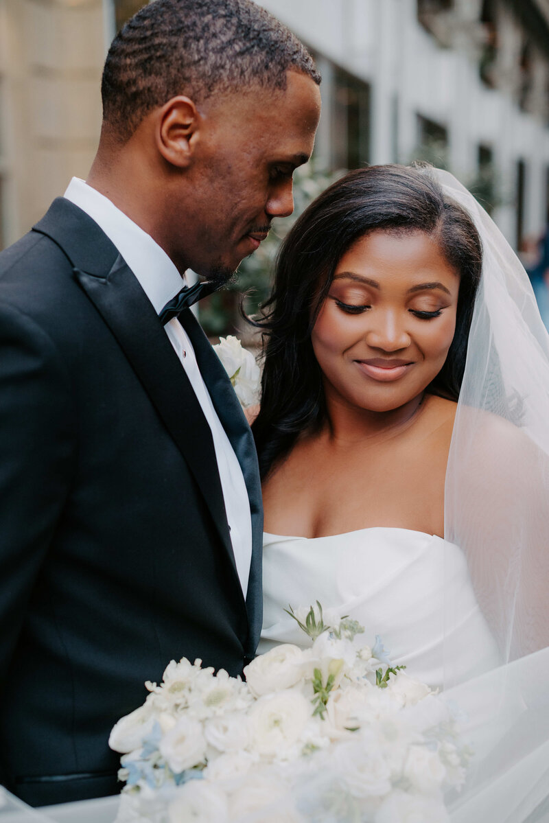 Intimate wedding portrait of a bride and groom, with the groom in a black tuxedo leaning toward his bride in a strapless gown holding a bouquet of white flowers