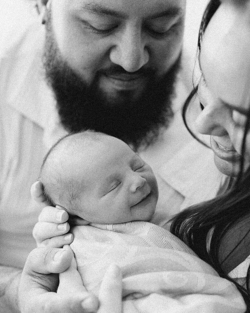 close up of a newborn baby smiling, swaddled, with both parents smiling in love at their new baby, Perth newborn in home session