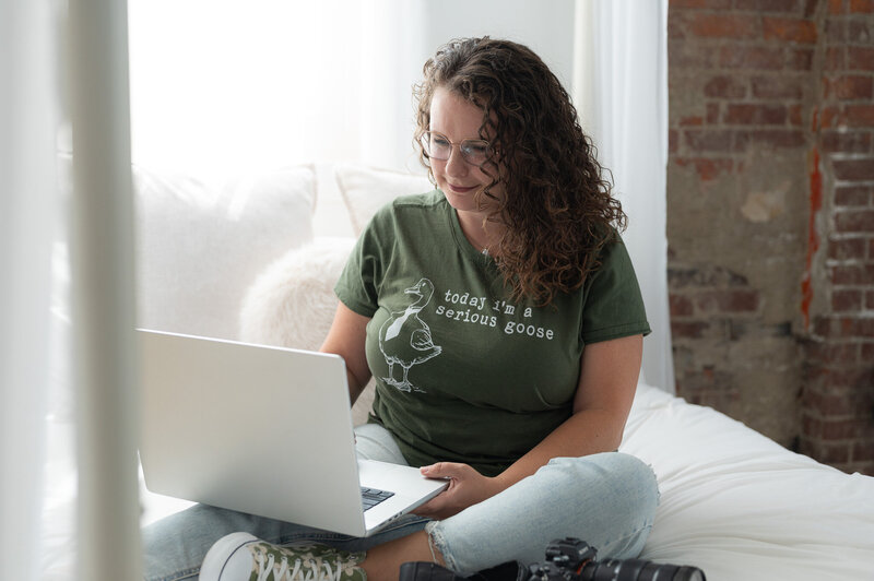 Emma Males smiling on a bed with her camera and laptop, representing connection and creativity in her photography community.