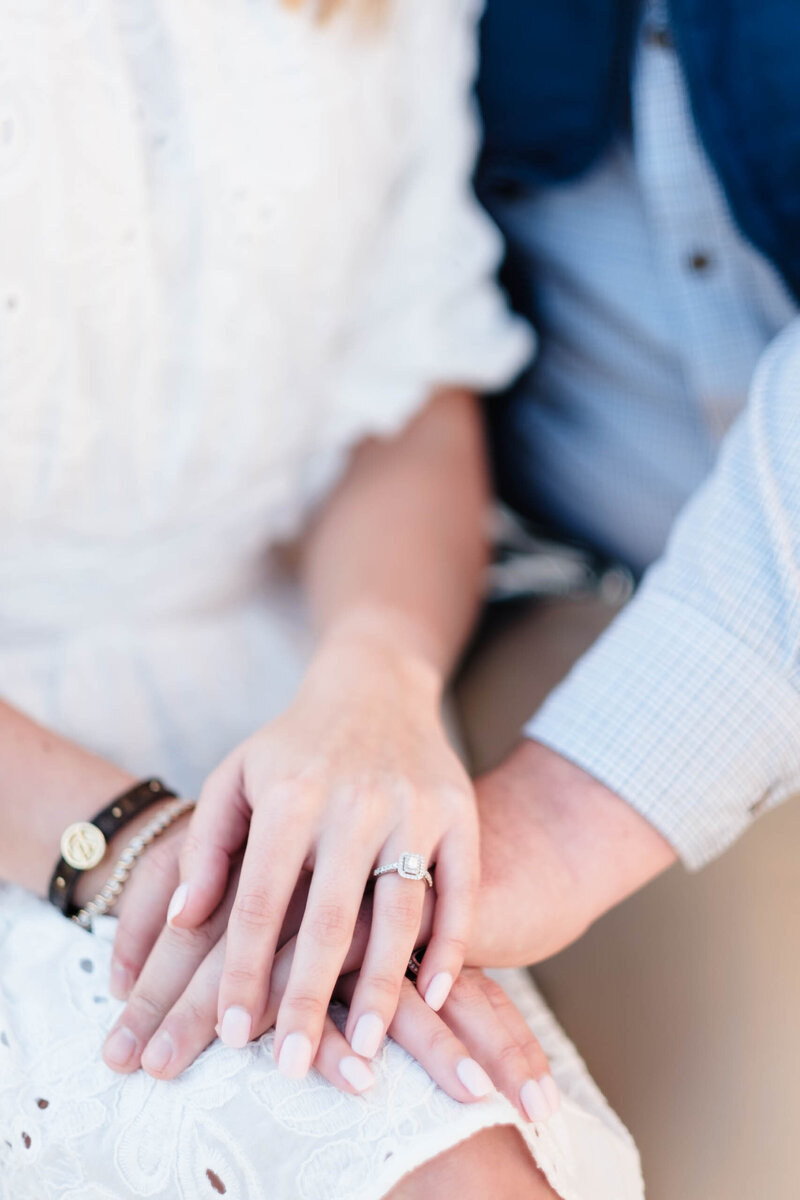 A close-up of a bride-to-be’s hand adorned with a stunning engagement ring, gently resting on her fiancé’s hand. The soft focus and natural lighting create a romantic, timeless feel, capturing the love and connection celebrated through Alabama wedding photography.