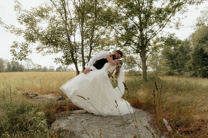 Groom dipping the bride for a kiss in a field.