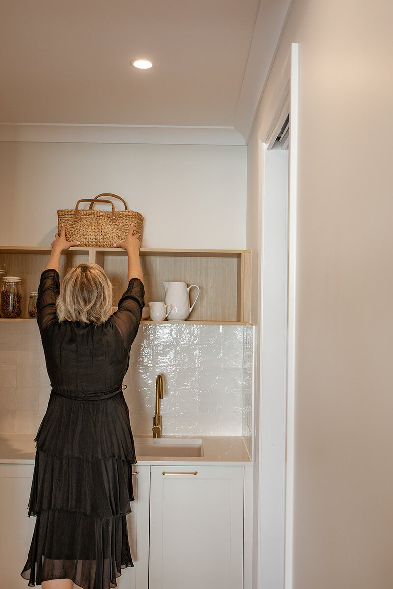 Lady putting a basket on shelf in kitchen