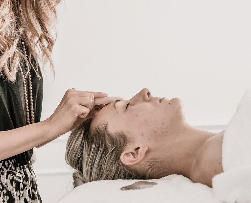 Woman blissed out receiving a relaxing Gua Sha gemstone facial massage.