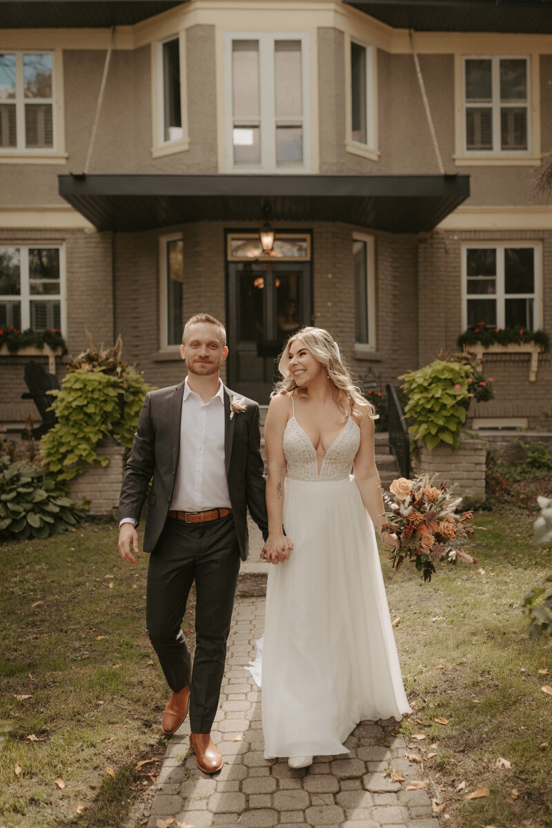 bride and groom holding hands in front of house