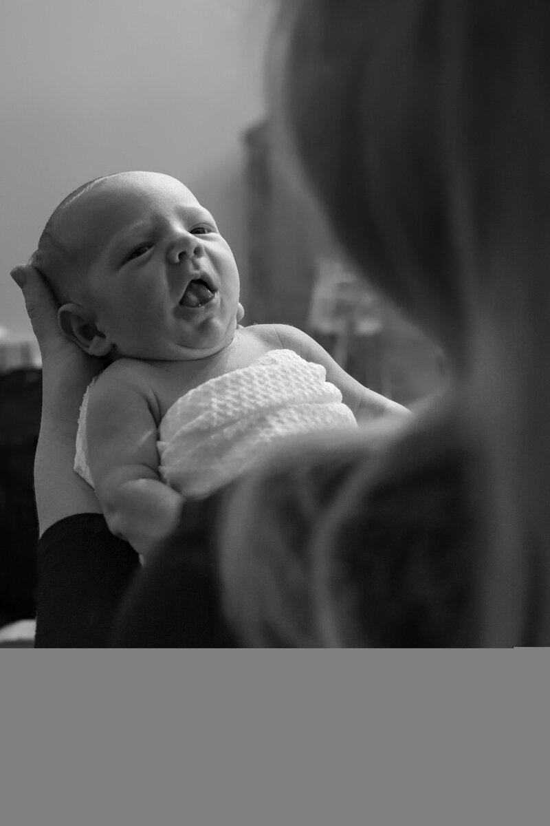 Newborn baby looking up at his mother, taken from behind her shoulder by lifestyle newborn photographer in Tifton