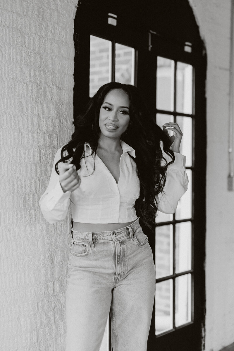 Black and white photo of Tiara in a white top and jeans touching her hair