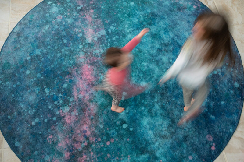Two children are playing on a blue and pink rug.