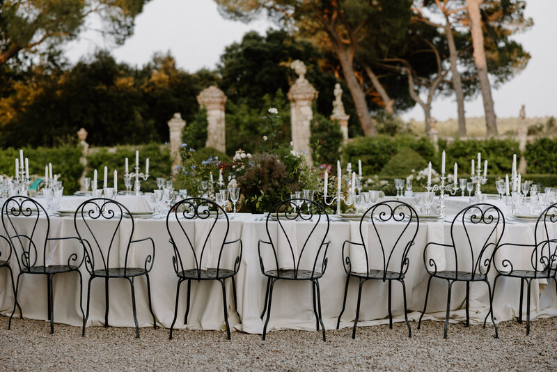 A white wedding reception table with candles and small florals set up outside 