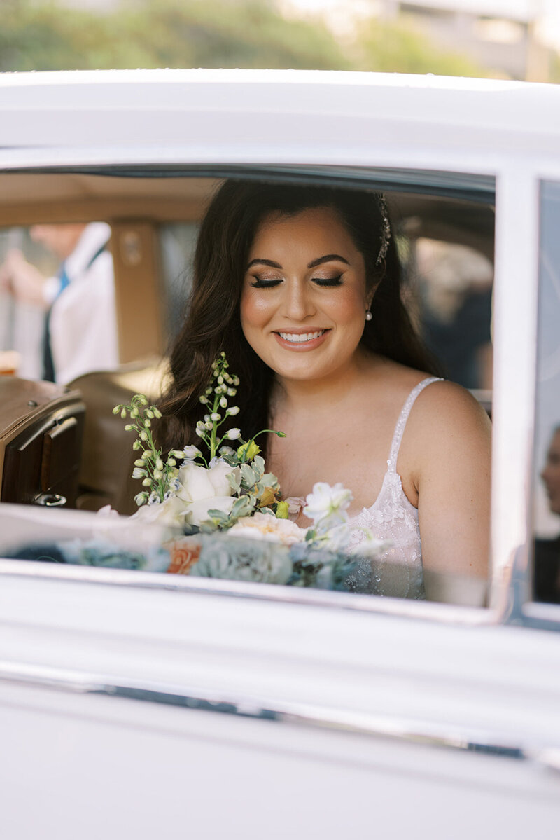 bride holding a floral bouquet and riding in classic car