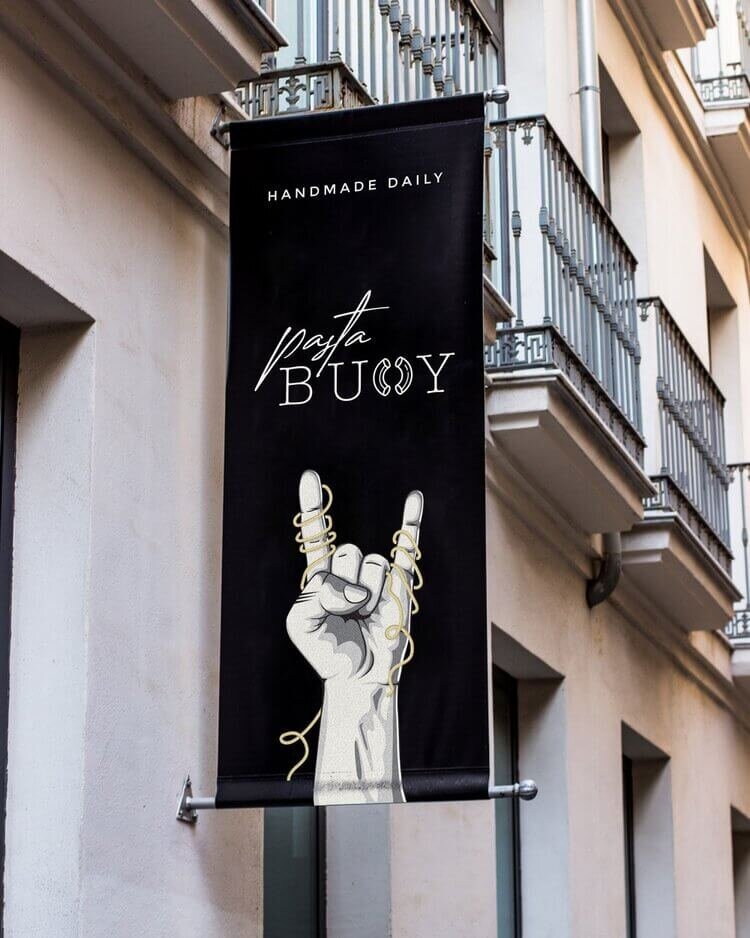 A Pasta Buoy street-side banner with the brand’s logo, featuring a hand making a playful gesture with intertwined pasta. The bold black-and-white design hangs on the exterior of a modern building, drawing attention to the fun and creative vibe of the restaurant.