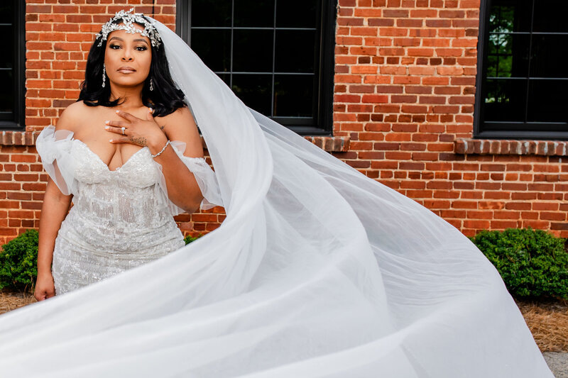 This fashionable Black bride stuns in an off-the-shoulder wedding dress, with a dramatic headpiece and flowing veil, at The Cotton Press in Little Mountain, SC. A breathtaking image of modern bridal elegance.