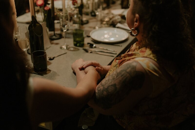 Two people holding hands at a Bellingen wedding table. One has tattoos and  piercings.