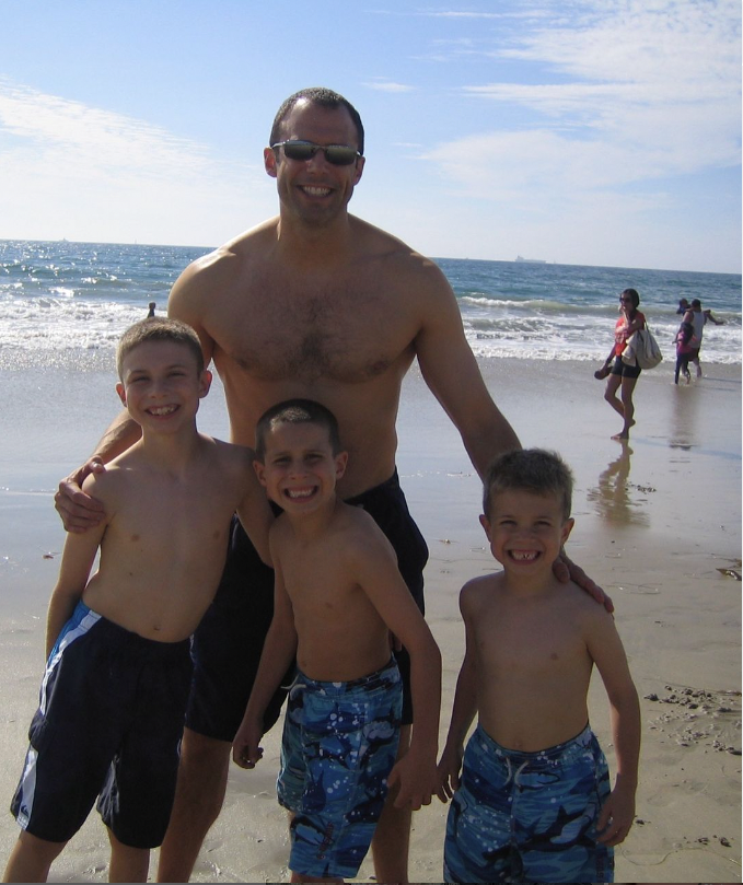 Jason lewis with 3 small boys at the beach.  Ocean in background