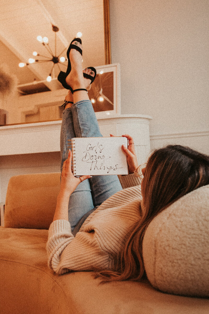 Girl laying on couch with legs in the air and holding a book
