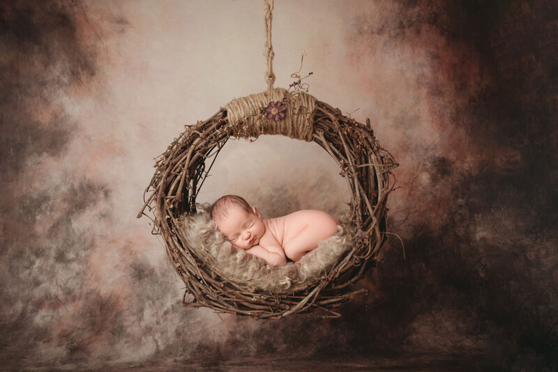 newborn baby boy laying on tummy in round hanging nest prop with brown fur against brown canvas backdrop