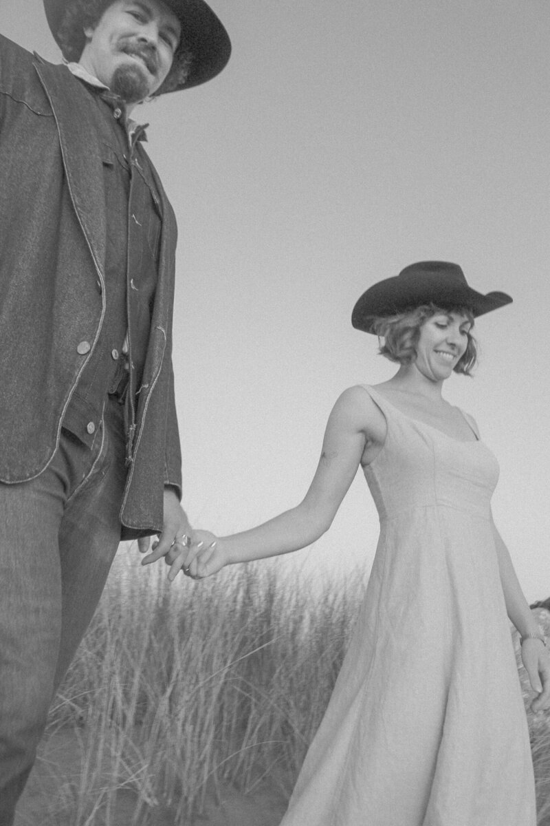 cowboy aesthetic playful engagement photos in san francisco california with couple kissing in the dunes