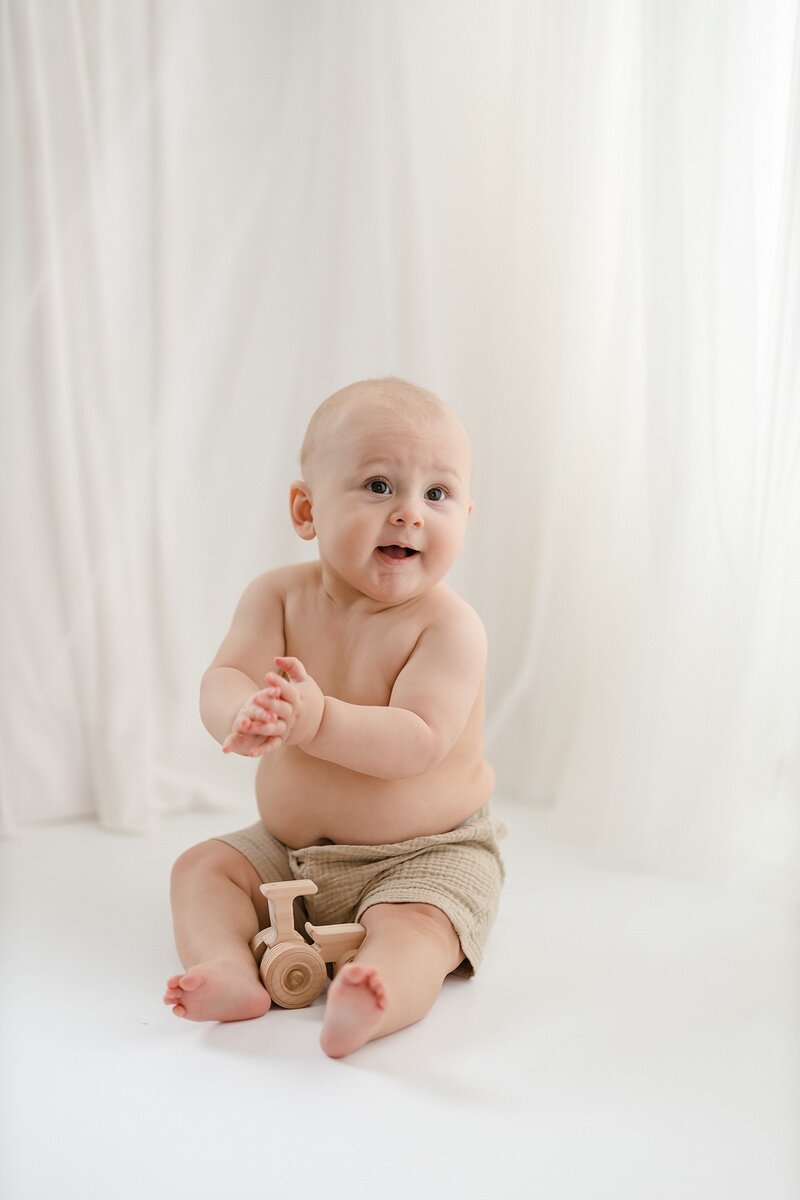 Chunky baby boy with bare belly clapping hands in front of white curtains - adorable milestone photography by Glean and Co Boise studio
