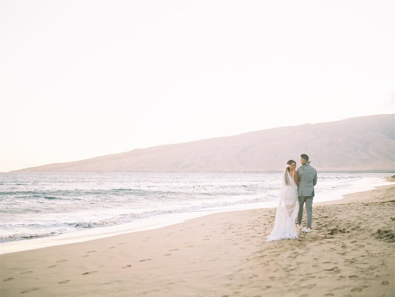 The newlyweds stand on a beach in Maui during sunset, with mountains in the background. This wedding was planned and designed by Thater Made, a luxury wedding and event producer based in San Diego, CA.