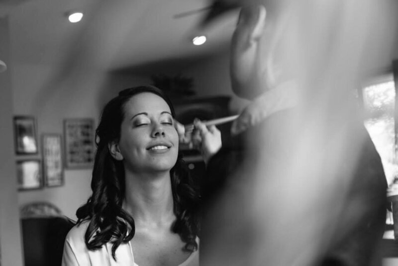 A bride leans into her makeup application with  her eyes closed and a soft smile on her face. She is relaxed and calm.