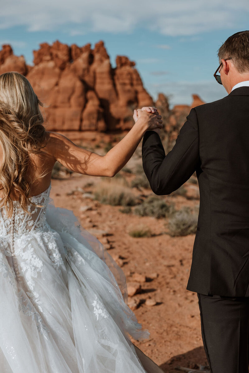 bride and groom holding hands while walking through the desert