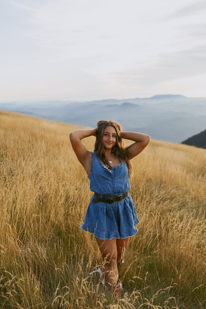 girl in blue dress standing on beach with forest in the background in an oregon senior portrait