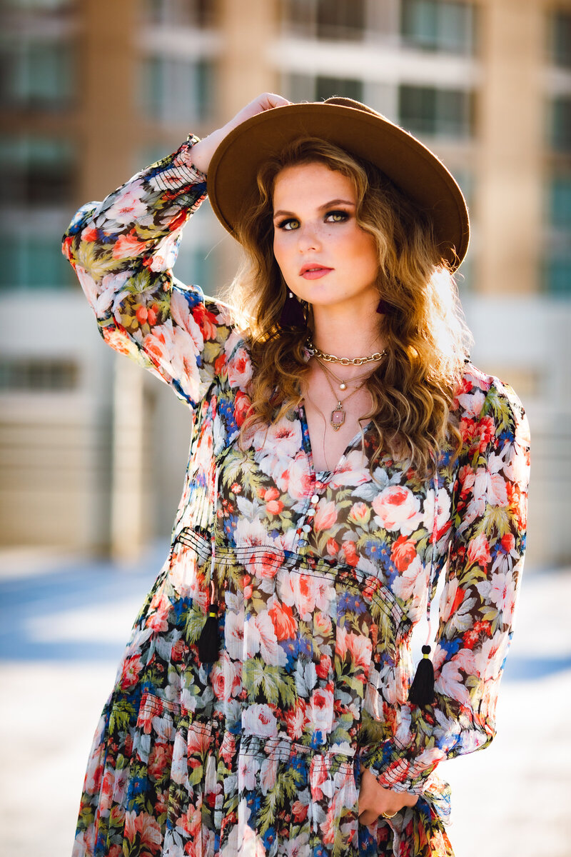 Highschool senior girl posing with flowy flower dress and hat  during golden hour