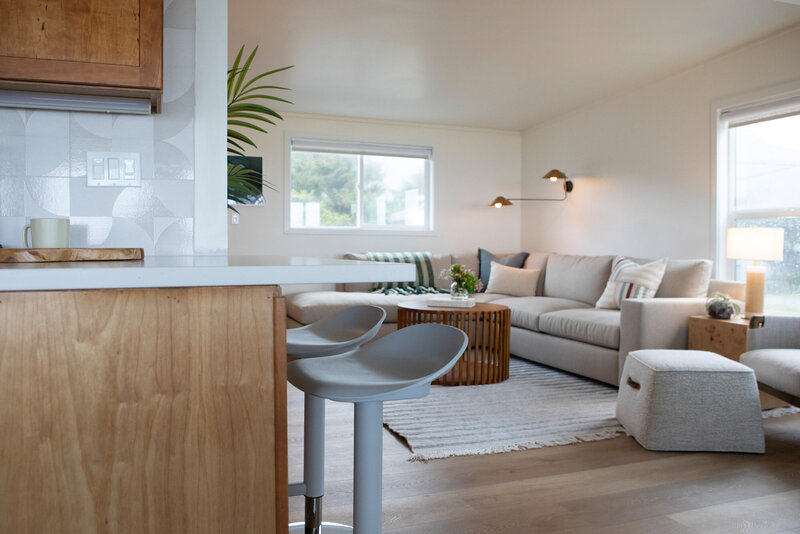 Stylish living room details from a short term rental renovation featuring a beige couch, wooden coffee table and blue bar stools.