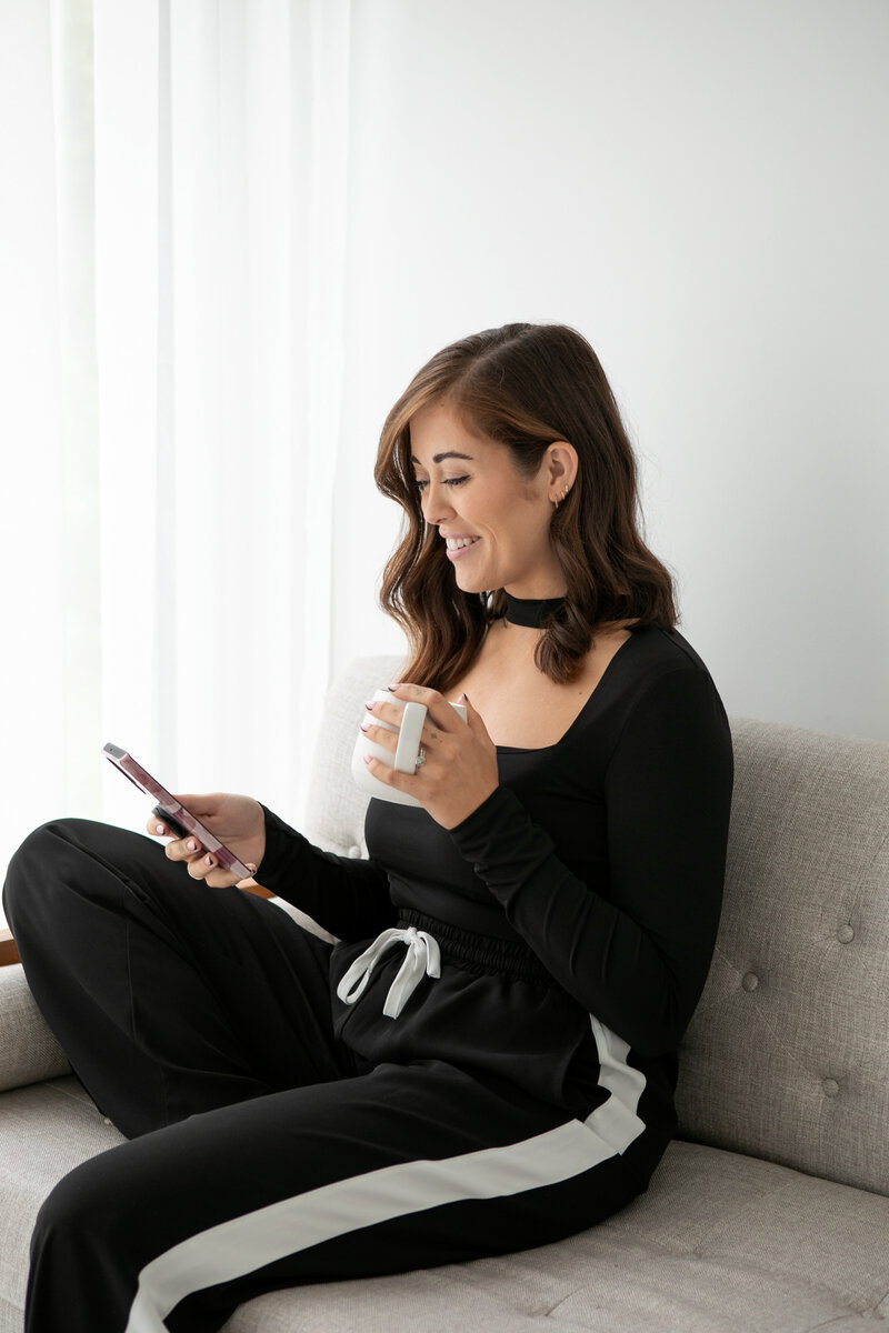 LADY ON SOFA LOOKING AT PHONE WITH A CUP OF TEA