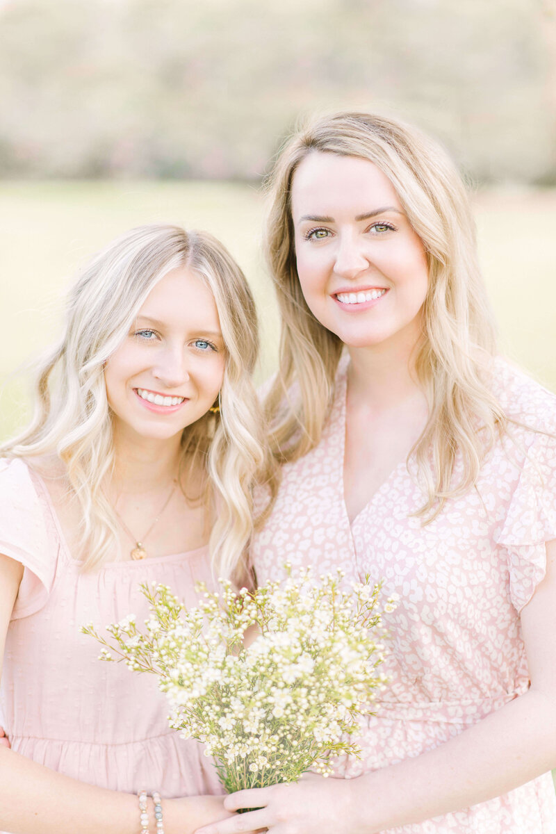 A mother and daughter hold a bouquet of white wild flowers and smile for the camera