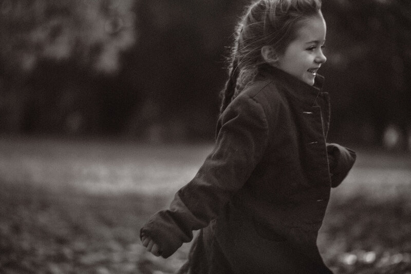 A black and white portrait of a little girl with a braid in her hair running away smiling. By Brittany Danielle