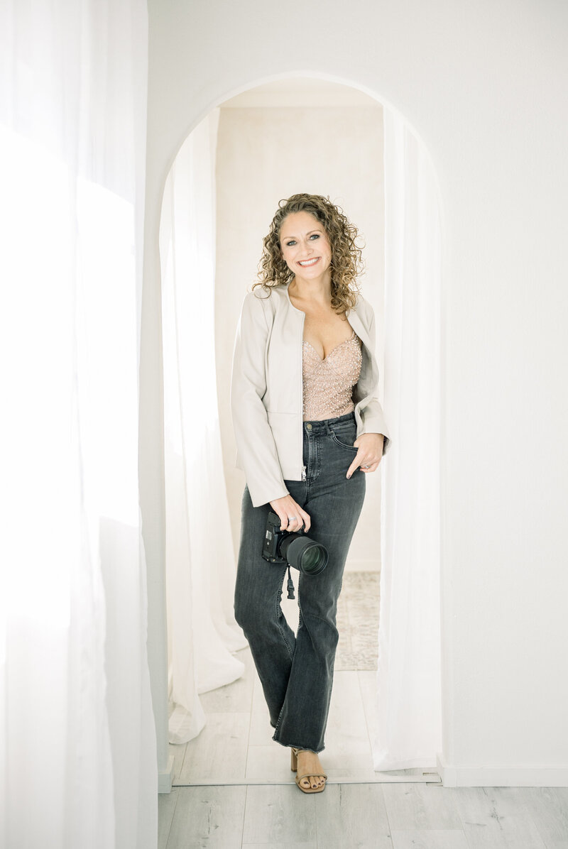 Boudoir photographer posed in her studio smiling with her camera ready to shoot in Orange County, California